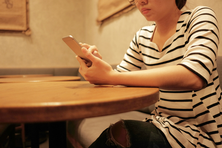 young woman using mobile phone and waiting alone in restaurant background with copy spaceの写真素材