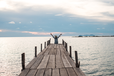 traveler young woman in sitting alone on wood bridge has sunset and sea backgroundの写真素材