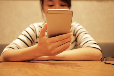 young woman using mobile phone and waiting alone in restaurant background with copy spaceの写真素材