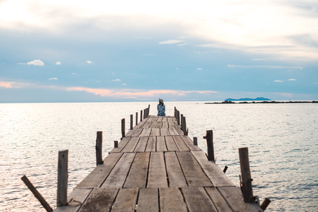 traveler young woman in sitting alone on wood bridge has sunset and sea backgroundの写真素材