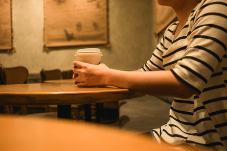 lifestyle background young woman holding coffee glass sitting alone in restaurant with copy space. image for food, person, beverage, portrait conceptの写真素材
