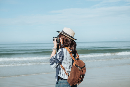 traveler young woman in casual dress holding camera and take photo with backpack standing alone on beach has sea backgroundの写真素材