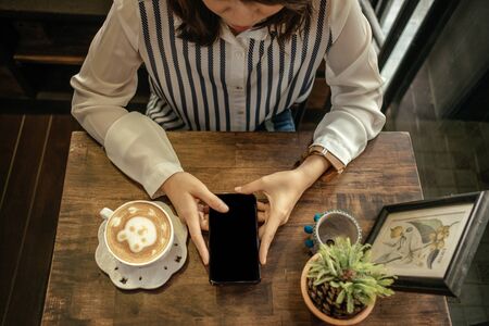 top view. young woman sitting in restaurant and using mobile phone has coffee cup with latte art and...