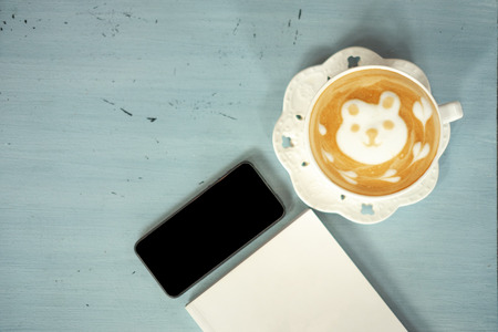 top view cup of coffee, mobile phone and blank notebook placed on wooden work table backgroundの写真素材