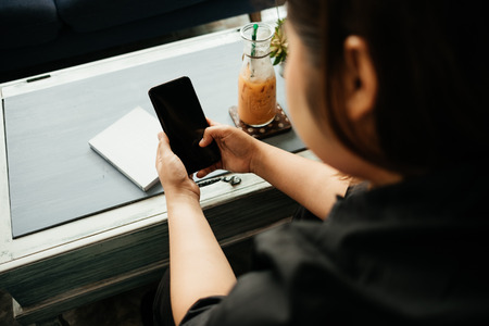 young businesswoman sitting in workplace and using mobile phone has notebook and beverage on table backgroundの写真素材