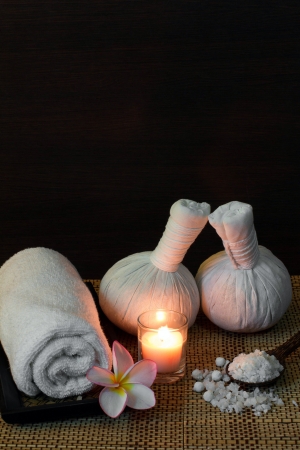 Thai spa massage setting with towel, frangipani, herbal compress balls and bath salt on spoonの写真素材