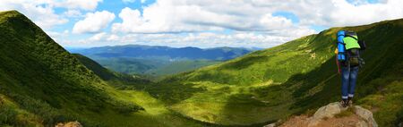 backpacker standing in front of mountain range and valley taken on panorama and standing backward to the cameraの写真素材
