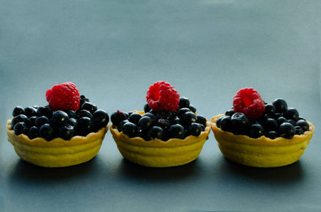 three blueberry and raspberry tarts on dark backgroung still life warm toning space for textの写真素材