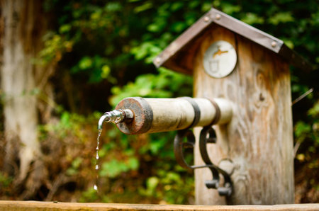 drinking water drops from a sring tap outdoor in park. the tap is wooden and old. closeup vertical composition. ecological concept of saving water and natural resourcesの写真素材