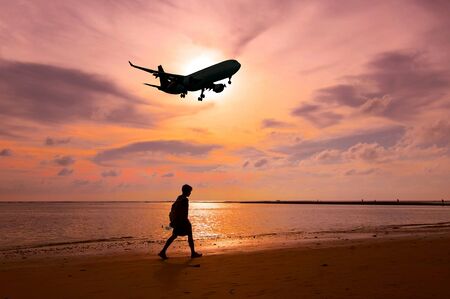 Man walking on the beach during sunset and airplane is landing to airportの素材