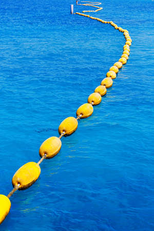 curves line of yellow buoys in clear blue seaの写真素材