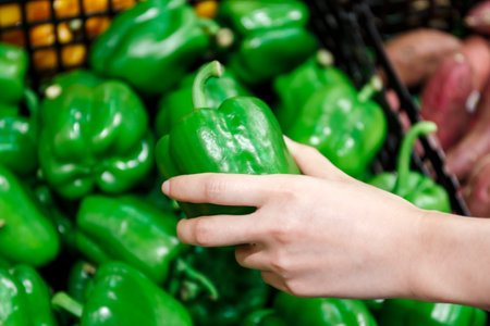 woman hand picking ripe green bell pepper in supermarketの写真素材