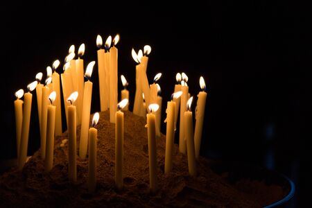 Many candles give warm yellow light in black backgroundの写真素材