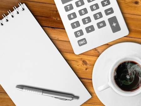 White calculator and white note paper with pen and white cup of hot coffee on wood tableの写真素材