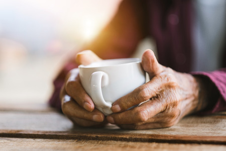 Hands of old man holding cup of coffee on the wood table.vintage toneの写真素材