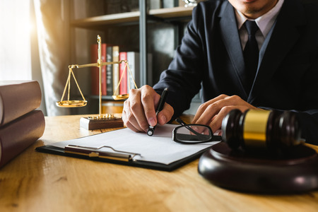 justice and law concept.Male judge in a courtroom  the gavel, working with smart phone and laptop and digital tablet computer on wood table in morning lightの写真素材