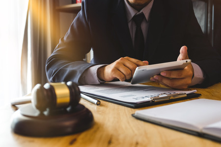 Justice and law concept.Male judge in a courtroom with the gavel, working with, digital tablet computer and smartphone docking keyboard, eyeglasses, on table in morning lightの写真素材