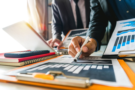 Businessman hand using laptop and tablet with social network diagram and two colleagues discussing data on desk as concept in morning light.の写真素材