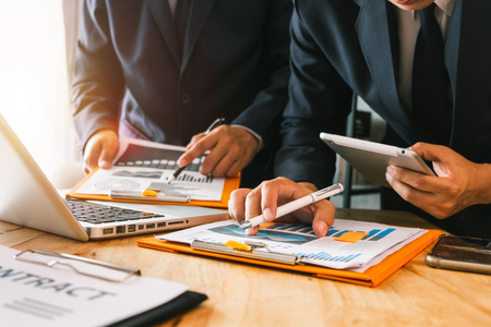 Business documents on office table with smart phone and calculator digital tablet and graph business with social network diagram and two colleagues discussing data working in the officeの写真素材