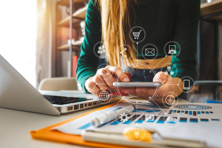 Woman using smart phone for mobile payments online shopping,omni channel,sitting on table,virtual icons graphics interface screen in morning lightの写真素材