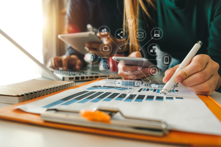 Business documents on office table with smart phone and calculator digital tablet and graph business with social network diagram and two colleagues discussing data working in the officeの写真素材