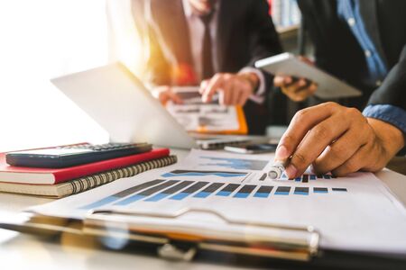 Business documents on office table with smart phone and calculator digital tablet and graph business with social network diagram and two colleagues discussing data working in the officeの写真素材