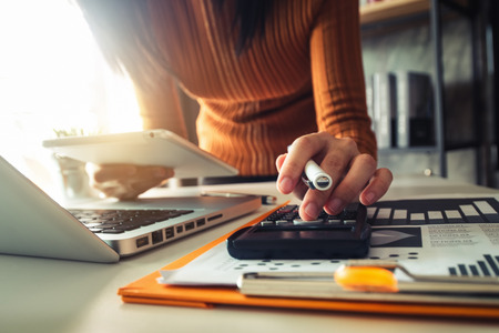 Businessman hands working with finances about cost and calculator and laptop with tablet, smartphone at office in morning lightの写真素材
