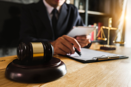 justice and law concept.Male judge in a courtroom  the gavel, working with smart phone and laptop and digital tablet computer on wood table in morning lightの写真素材