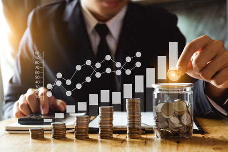 businessman holding coins putting in glass with using smartphone and calculator to calculate  concept saving money for finance accountingの写真素材