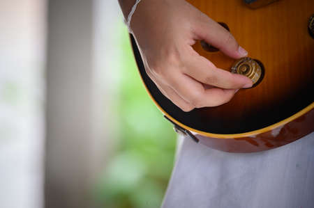 Woman's hand adjusting thevolume and tone of a brown guitar.