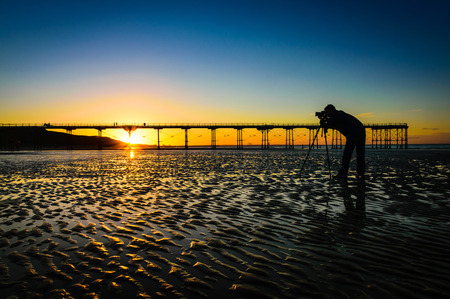 Silhouette of a photographer on beautiful sunset or sunrise at pier Saltburn by the Sea, North Yorkshire UK.の写真素材