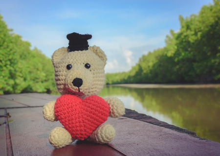Teddy Bear with red heart sitting on wooden bridge near the river - vintage toneの写真素材