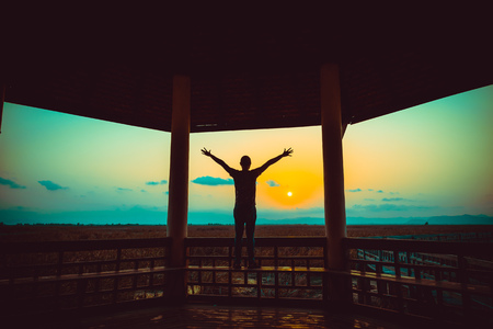 Happy free man silhouette in wooden pagoda during sunset. Vintage toneの写真素材