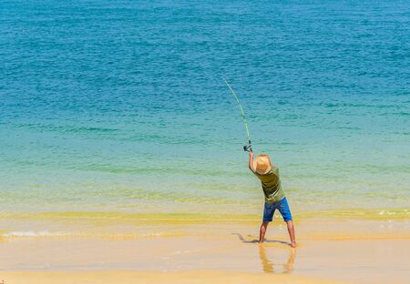 Young boy fishing rod on sunny beachの写真素材