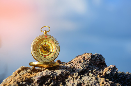 Analogical compass abandoned on the rocks with blurred sea background.