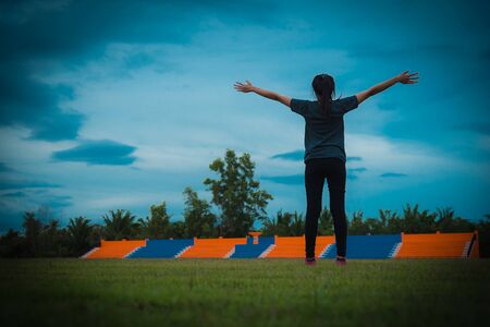 Woman pulls hands to the sky on green grass in stadium. Vintage tone.の写真素材