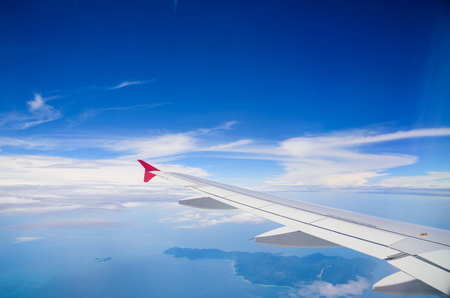 Wing of airplane flying above the clouds in the blue sky background.