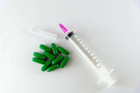 Empty medical syringe, needle and green pills isolated on a white background.の写真素材