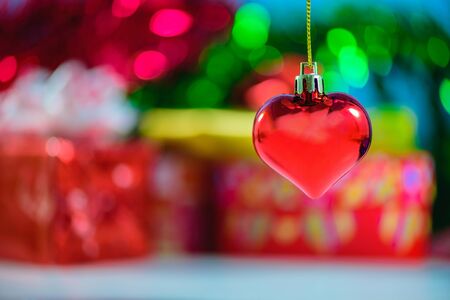 Christmas heart shaped red ball and blurred Christmas decorations box with bokeh background.の写真素材
