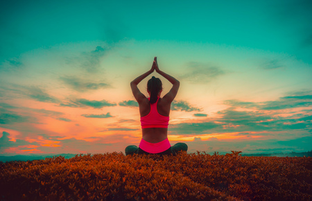 Silhouette young woman practicing yoga on the beach at sunset.の写真素材