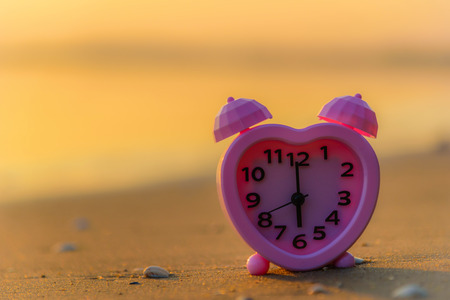 Pink clock on the beach at sunset. Summer vacation travel concept.の写真素材