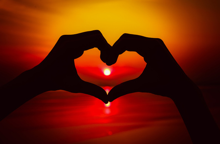 Silhouette hand in heart shape with sunset in the middle and sea background. Vintage toneの写真素材