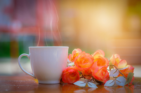 White coffee cup and rose flowers on wooden table with blurred background.の写真素材