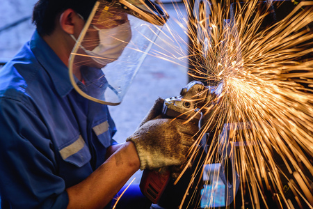 Heavy industrial worker used electric wheel grinding on steel structure in steel factory with...