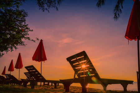 Beach bed and red umbrella on tropical beach at sunset with sun flare.の写真素材
