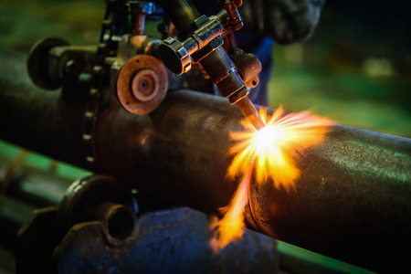 Worker cutting steel pipe with acetylene welding cutting torch and bright sparks in steel construction industry.の写真素材