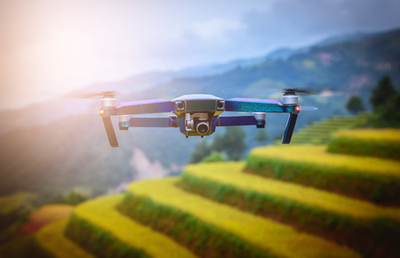 Modern RC Drone / Quadcopter with camera flying on rice fields terraced at sunset in Mu Cang Chai,...