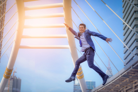 Portrait of business man jumping with arms up celebrate on blurred city background. Business success...