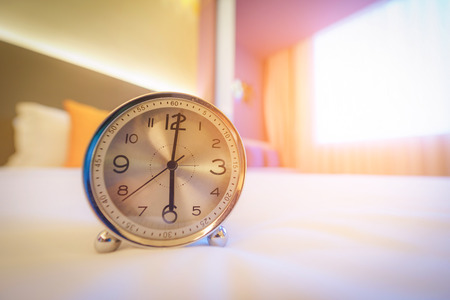 Alarm clock on the bed in morning time with sunlight.の写真素材