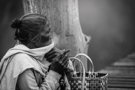 MANDALAY, MYANMAR - DECEMBER 11, 2017 : Old wrinkled woman smokes a cheroot cigar on U Bein wooden bridge in Mandalay, Myanmar. Black and white toneのeditorial素材